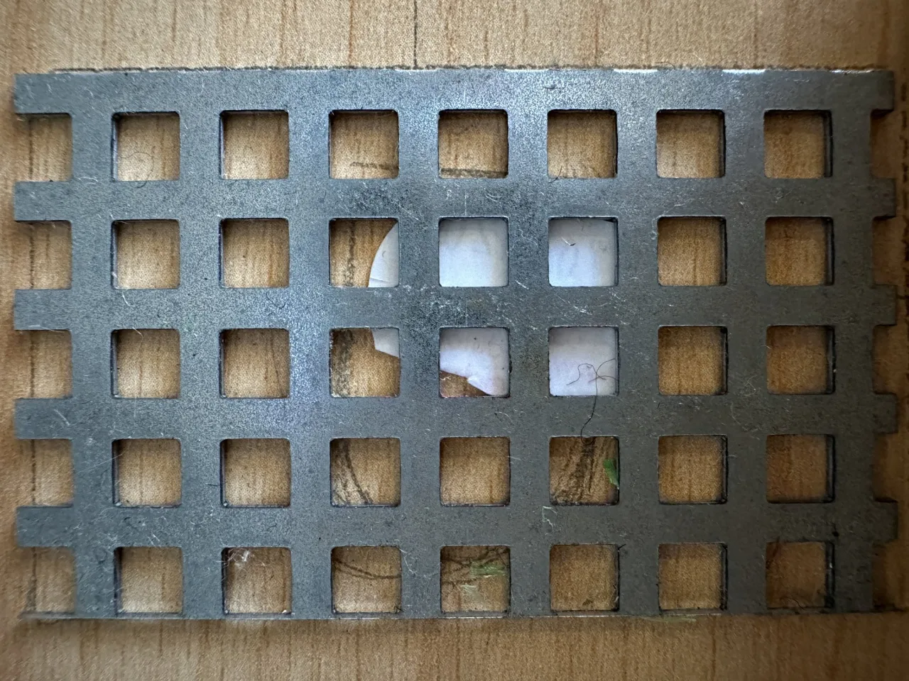 Photograph of material_0701420 — a perforated grid panel — the same material being pressed below.